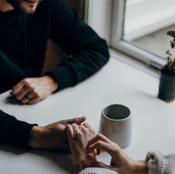 Two people holding hands across a table, discussing an intimate relationship dynamic